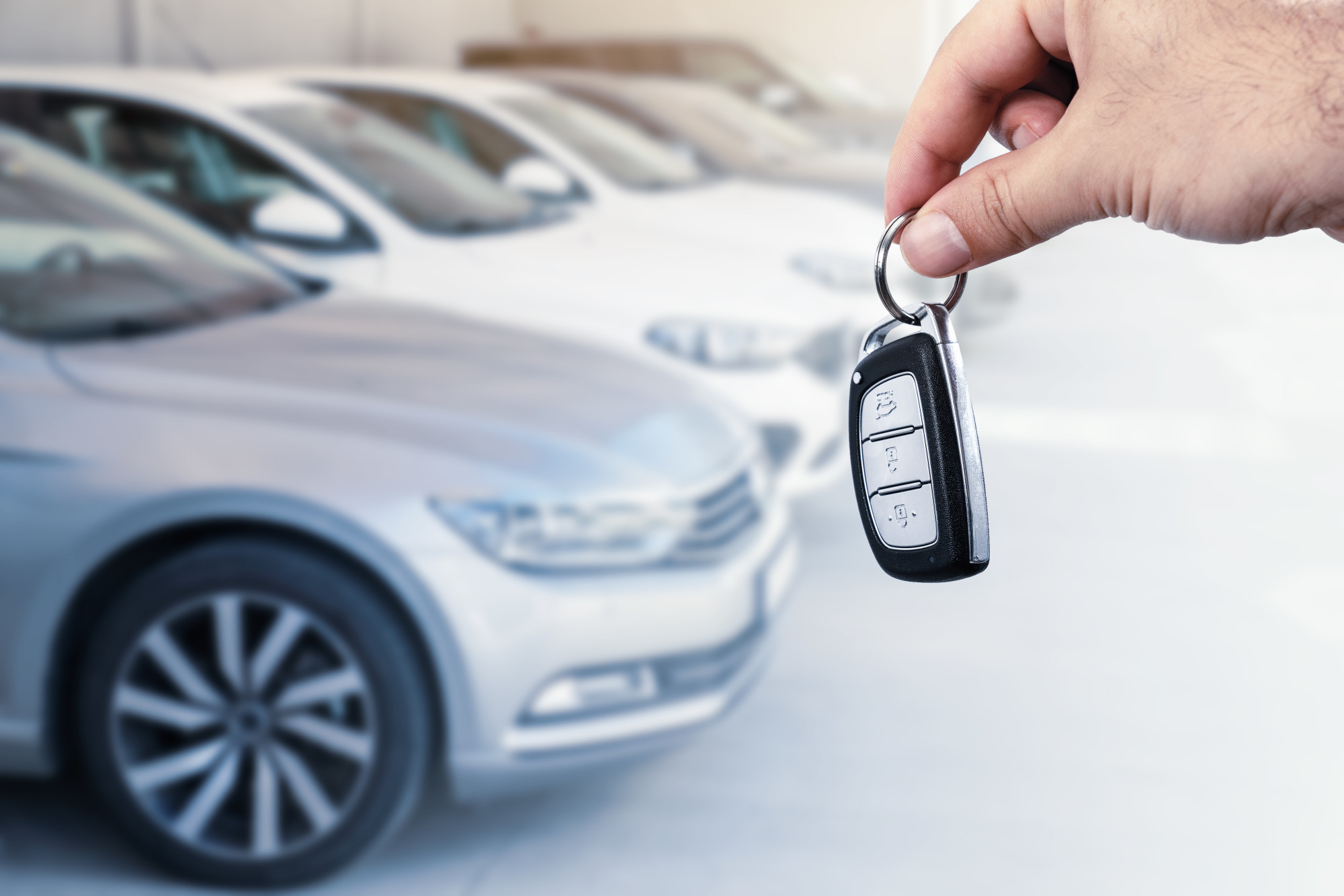 hand holding car key in front of row of cars